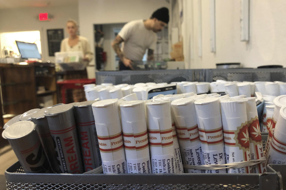 In this photo taken Sept. 20, 2019, employees at the marijuana retailer Bridge City Collective in Portland, Ore., can be seen setting up the store for the day behind a row of marijuana products for sale there. Vaping products are taking a hit as health experts scramble to determine what’s causing a mysterious lung disease. Many patients say they used vapes containing marijuana oil, but some patients say they smoked nicotine-only vapes. (AP Photo/Gillian Flaccus)