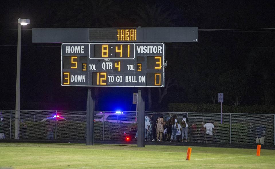 A group gathers around one of the victims of a shooting at Palm Beach Central High School. Two adults were shot on Aug. 17, 2018 at a football game between Palm Beach Central and William T. Dwyer high schools, authorities said. The gunfire sent players and fans screaming and stampeding in panic during the fourth quarter of the game.