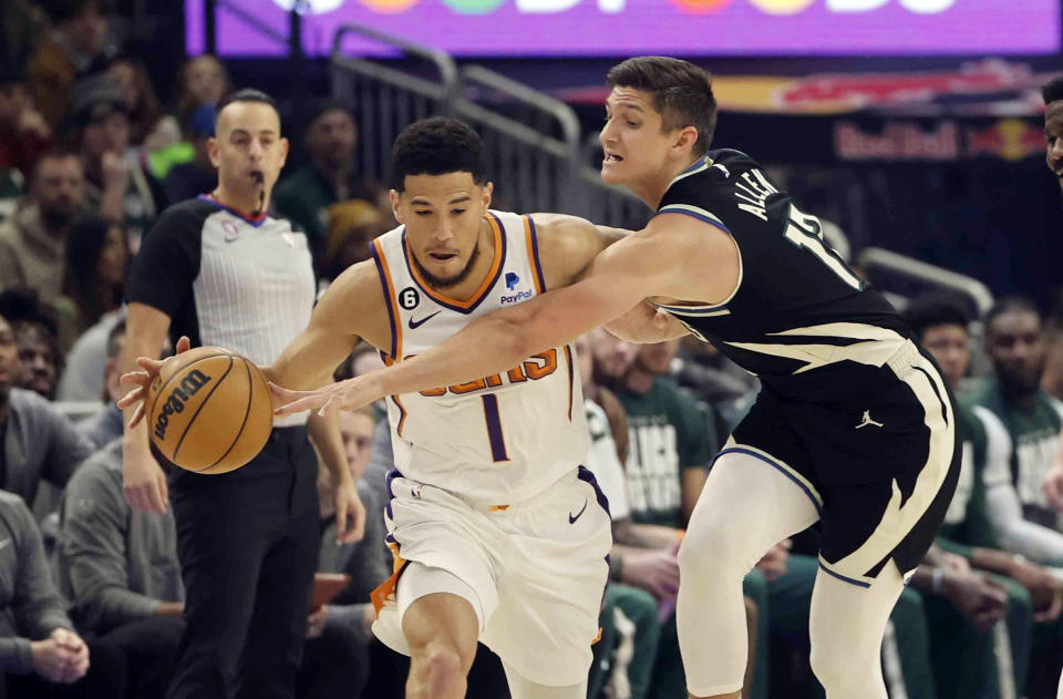 Milwaukee Bucks guard Grayson Allen (12) reaches in on Phoenix Suns guard Devin Booker (1) during the first half of an NBA basketball game Sunday, Feb. 26, 2023, in Milwaukee. (AP Photo/Jeffrey Phelps)