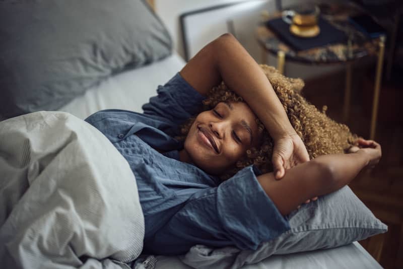 Beautiful woman lying on her bed sideways. She has her eyes close and she is smiling.