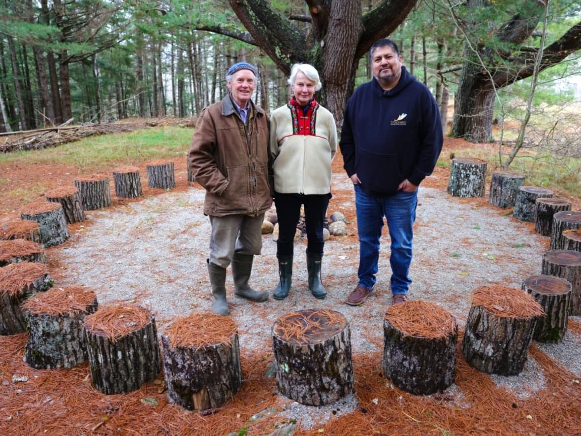 Jim and Margaret Drescher, the owners of Windhorse Farm since 1990, are shown with Chris Googoo, COO of Ulnooweg, which takes control of the property this week. The three stand in a circle created for sacred fires. (Jeorge Sadi/CBC - image credit)