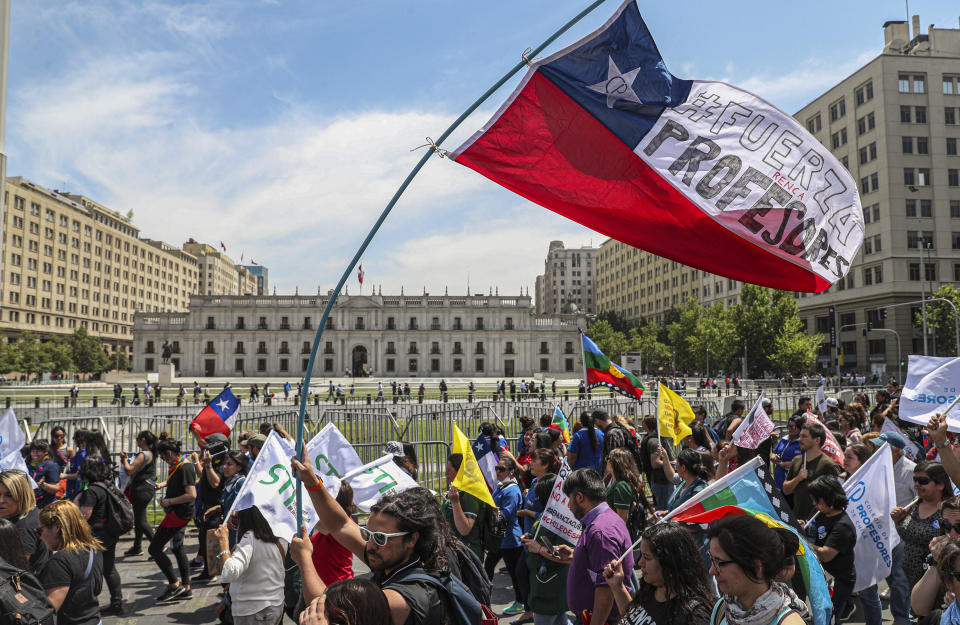 A teacher marches with a Chilean flag covered with the Spanish message: "Be strong professors." outside La Moneda presidential palace in Santiago, Chile, Monday, Nov. 11, 2019. A plan by Chilean President Sebastián Piñera's to draft a new constitution has been criticized by the opposition and even his own political ranks. Students in Chile began protesting nearly a month ago over a subway fare hike. (AP Photo/Esteban Felix)