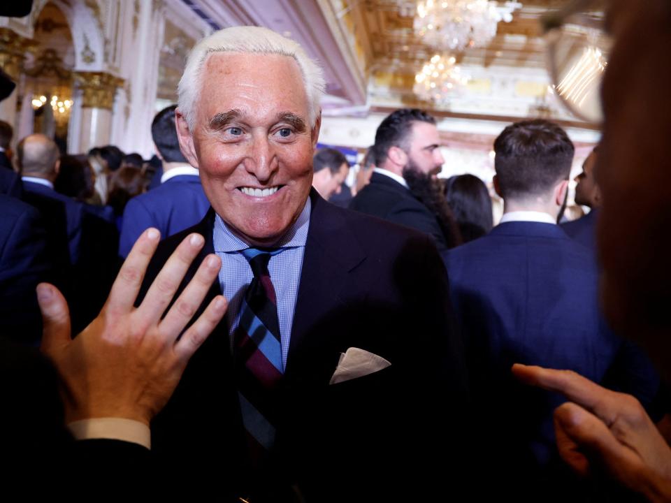 Roger Stone, with white hair and a blue suit