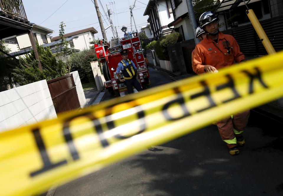 A police officer stands guard on the street in front of the site where a light plane went down in a residential area and burst into flames, in Chofu