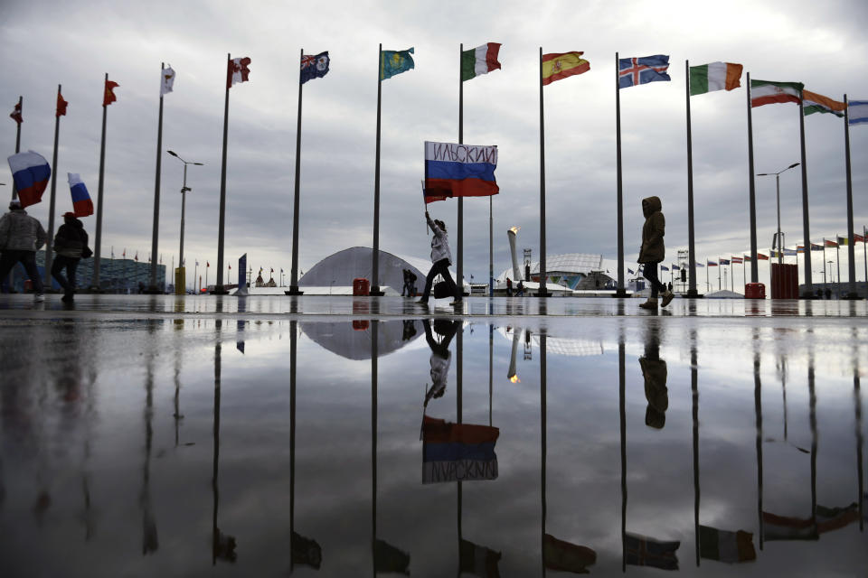 A fan is reflected in a puddle carrying the Russian flag past the Olympic cauldron at the 2014 Winter Olympics, Tuesday, Feb. 18, 2014, in Sochi, Russia. (AP Photo/David Goldman)