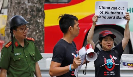 A Vietnamese policeman approaches anti-China protesters while they hold placards during a demonstration in front of the Chinese embassy in Hanoi