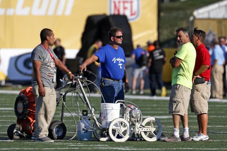 The ground crew at Tom Benson Hall of Fame Stadium check the turf after scraping the painted logo off the center of the field (AP)