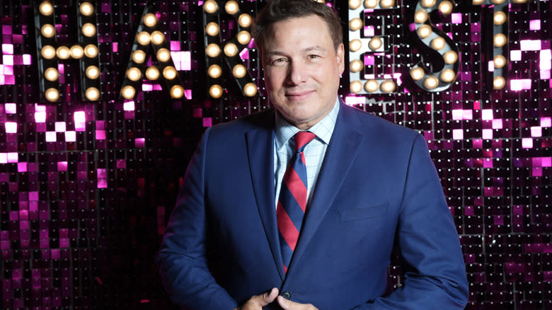 Rocco DiSpirito in suit in front of pink sparkly backdrop
