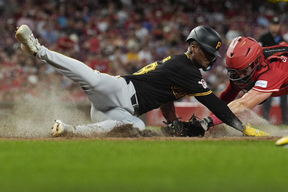 Pittsburgh Pirates' Michael A. Taylor dives safely past the tag by Cincinnati Reds catcher Tyler Stephenson to score in the sixth inning of a baseball game Tuesday, June 25, 2024, in Cincinnati. The Pirates won 9-5. (AP Photo/Carolyn Kaster)