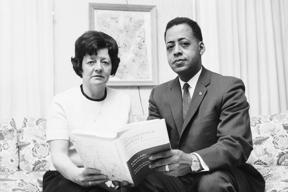 Betty and Barney Hill in a black-and-white photo hold a copy of their book together on a couch. 