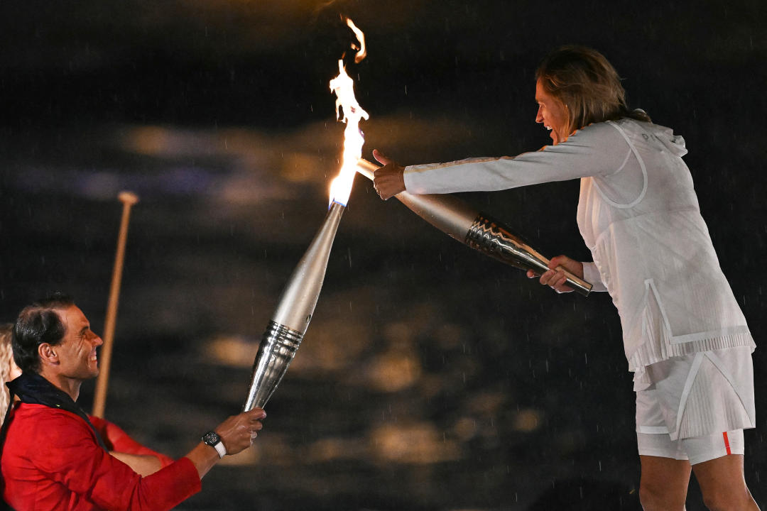 Spain's tennis player Rafael Nadal (L) hands over the Olympics torch to former French tennis player Amelie Mauresmo holding the torch during the opening ceremony of the Paris 2024 Olympic Games in Paris on July 26, 2024. (Photo by Kirill KUDRYAVTSEV / AFP) (Photo by KIRILL KUDRYAVTSEV/AFP via Getty Images)