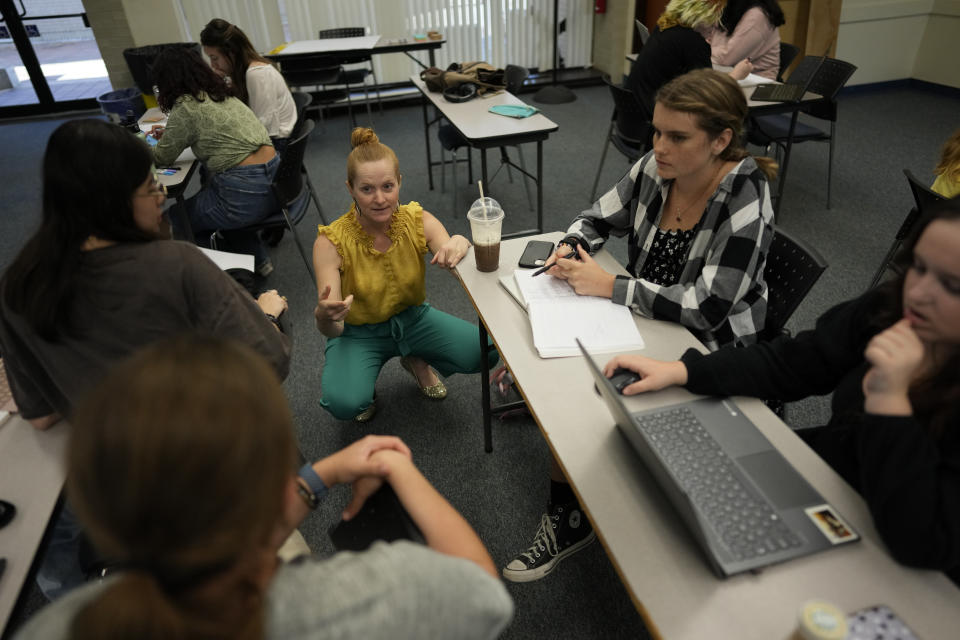 Jennifer Wells, center, director of writing at New College of Florida, checks in with students working on an in-class project, during her "Rhetoric of Walt Disney World" class, Thursday, March 2, 2023, in Sarasota, Fla. Wells says the school's small class sizes allow her to focus on student needs and get to know everyone in her classes, while the flexibility that students get to choose their classes and majors is unique, especially for a public liberal arts college. (AP Photo/Rebecca Blackwell)