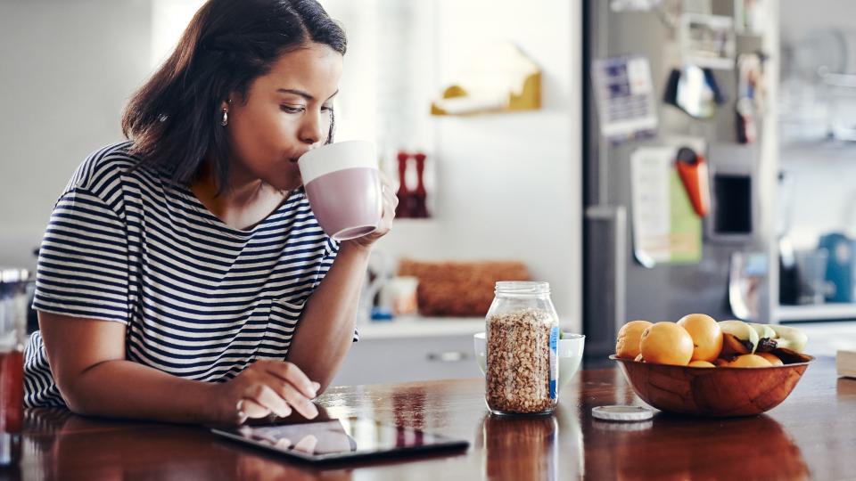 Shot of an attractive young woman drinking coffee while using a digital tablet at home.