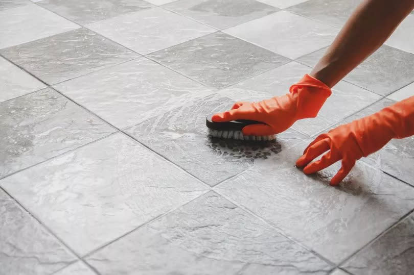 Hand of man wearing orange rubber gloves is used to convert scrub cleaning on the tile floor.