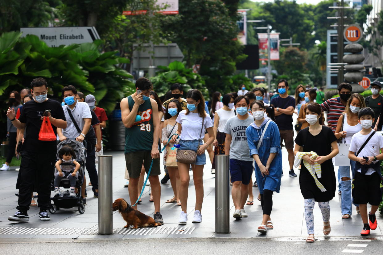 SINGAPORE - JUNE 20:  People wearing protective masks wait to cross a street at Orchard Road shopping belt on June 20, 2020 in Singapore. From June 19, Singapore started to further ease the coronavirus (COVID-19) restrictions by allowing social gatherings up to five people, re-opening of retail outlets and dining in at food and beverage outlets, subjected to safe distancing. Parks, beaches, sports amenities and public facilities in the housing estates will also reopen. However, large scale events, religious congregations, libraries, galleries and theatres will remain closed.  (Photo by Suhaimi Abdullah/Getty Images)