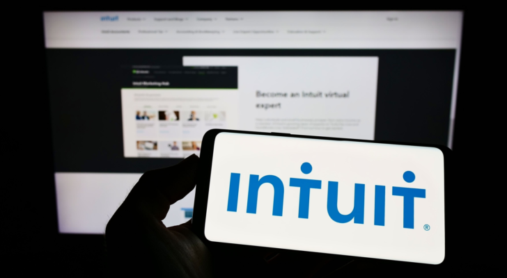 Person holding cellphone with logo of US financial software company Intuit Inc. (INTU) on screen in front of business webpage. Focus on phone display. Unmodified photo.