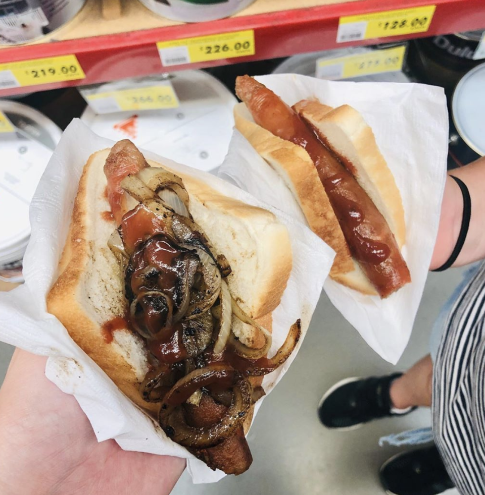 Two Bunnings Warehouse customers holding a sausage sandwich each inside the store