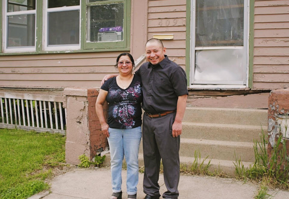 In this Saturday, May 23, 2020, photo provided by Cristobal Francisquez, his parents Paulina and Marcos Francisco pose for a photo in front of their house in Sioux City, Iowa. They bought the home after years of working in a meatpacking plant and other food processing jobs. (Cristobal Francisquez via AP)