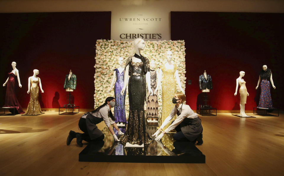 Gallery assistants handle a black and gold sequined 'Oscar' dress worm by Nicole Kidman, amongst other items on display at Christie's, from the archive of fashion designer L'Wren Scott before it is offered at auction, in London, Thursday June 10, 2021. (Jonathan Brady/PA via AP)