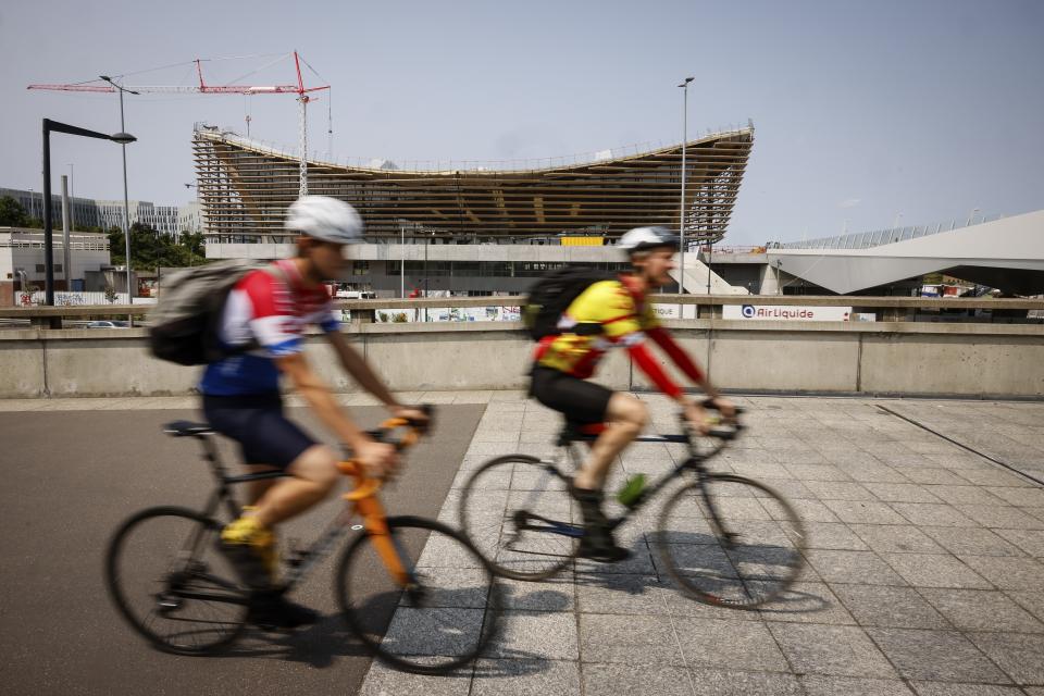 ARCHIVO - Ciclistas pasan frente al Centro Acuático de Saint-Denis, el 10 de julio de 2023. Será el escenario de la natación artística, clavados y polo acuático en los Juegos Olímpicos. (AP Foto/Thomas Padilla)