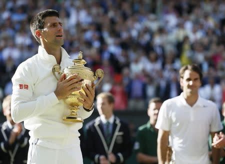 Novak Djokovic of Serbia holds the winner's trophy after defeating Roger Federer (R) of Switzerland in their men's singles finals tennis match on Centre Court at the Wimbledon Tennis Championships in London July 6, 2014. REUTERS/Stefan Wermuth