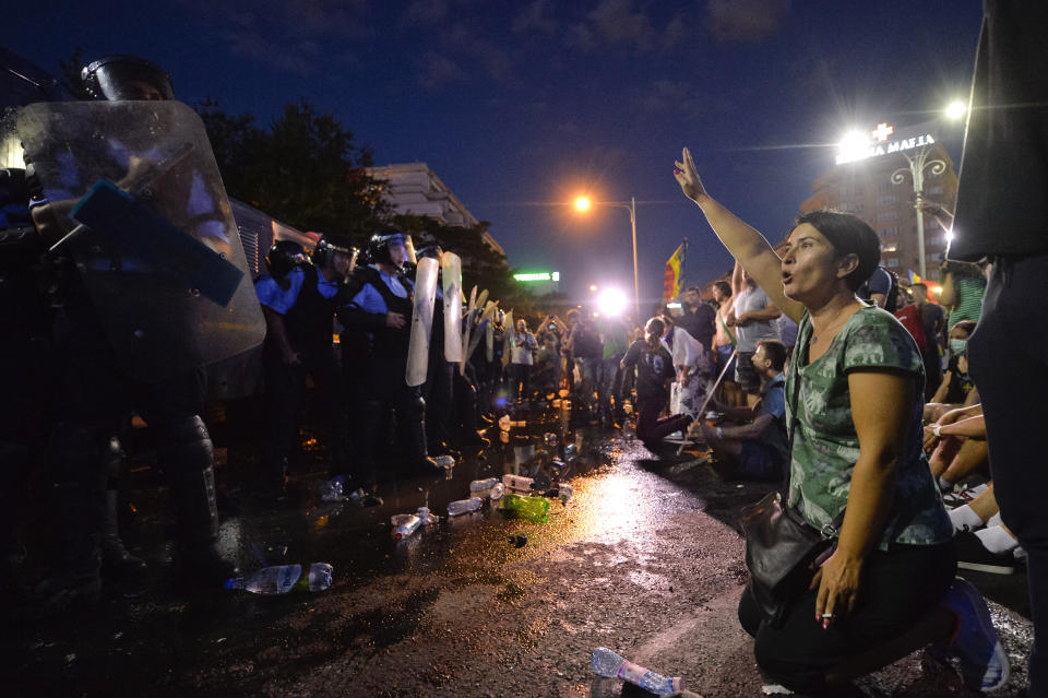 A woman shouts slogans in front of a riot police line during protests outside the government headquarters, in Bucharest, Romania, Friday, Aug. 10, 2018. Romanians who live abroad are staging an anti-government protest calling on the left-wing government to resign and an early election.(AP Photo/Andreea Alexandru)