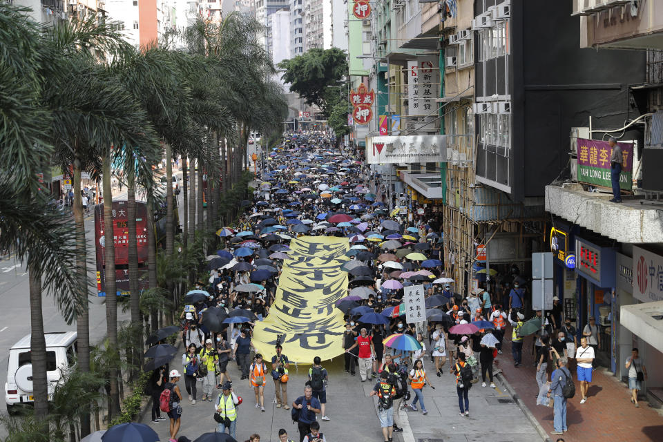Masked protesters walk next to a banner with the words "May Glory be to Hong Kong" in Hong Kong on Saturday, Oct. 5, 2019. All subway and trains services are closed in Hong Kong after another night of rampaging violence that a new ban on face masks failed to quell. (AP Photo/Vincent Thian)