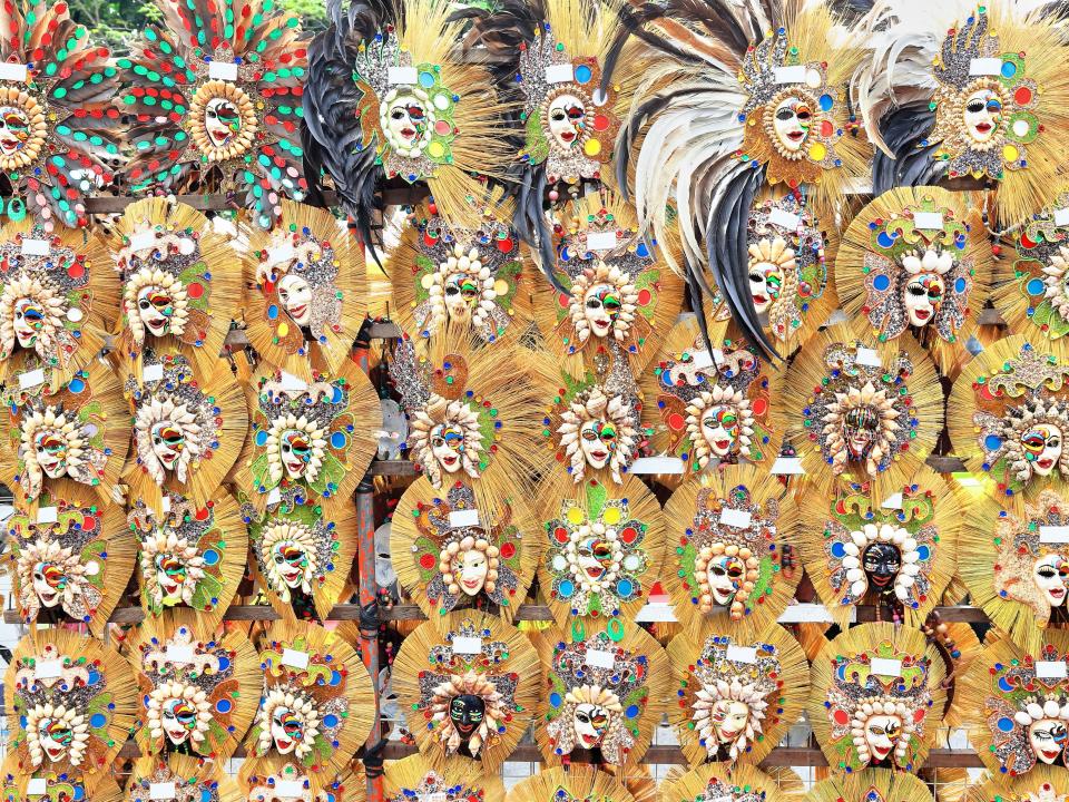 Several rows of decorative masks with large yellow plumes and brightly-colored accents