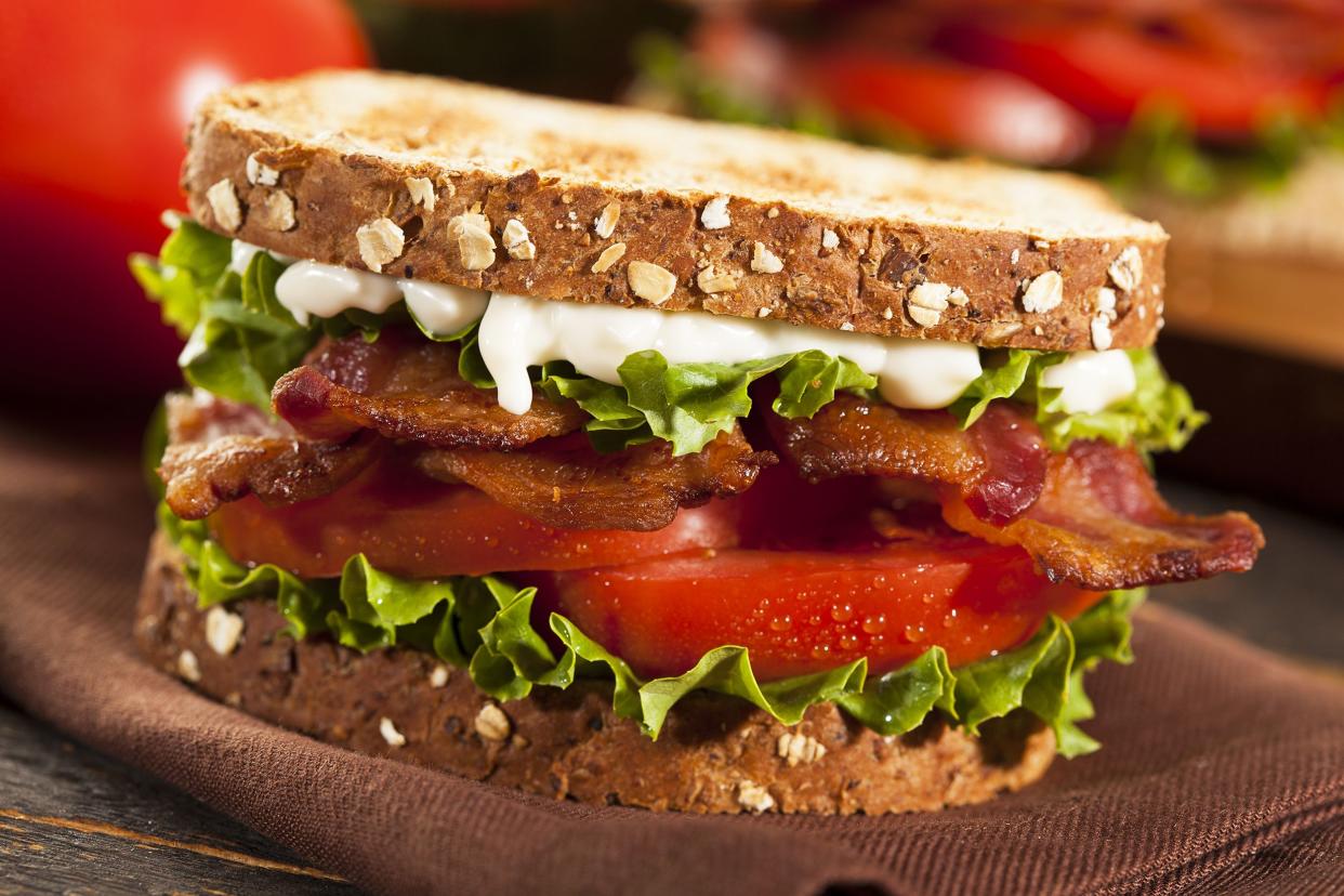 BLT sandwich, selective focus, on a brown napkin, on a rustic wooden table with ingredients blurred in the background