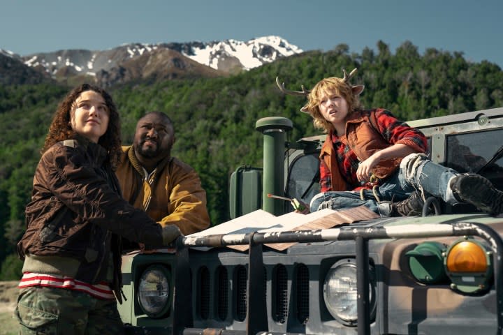 A young boy sits on a Jeep with two adults standing in front of him.