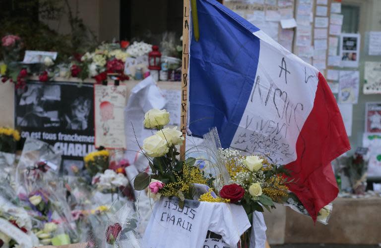 A flag flies among tributes on January 9, 2015 outside the Charlie Hebdo magazine offices in Paris for the victims of the January 7 massacre at the weekly, which left 12 dead