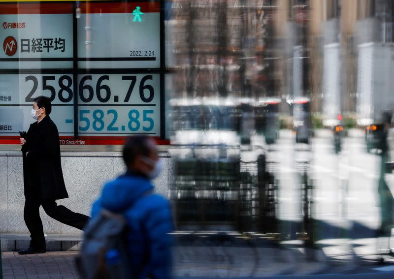 FILE PHOTO: Passersby wearing protective face masks walk past a stock quotation board, in Tokyo