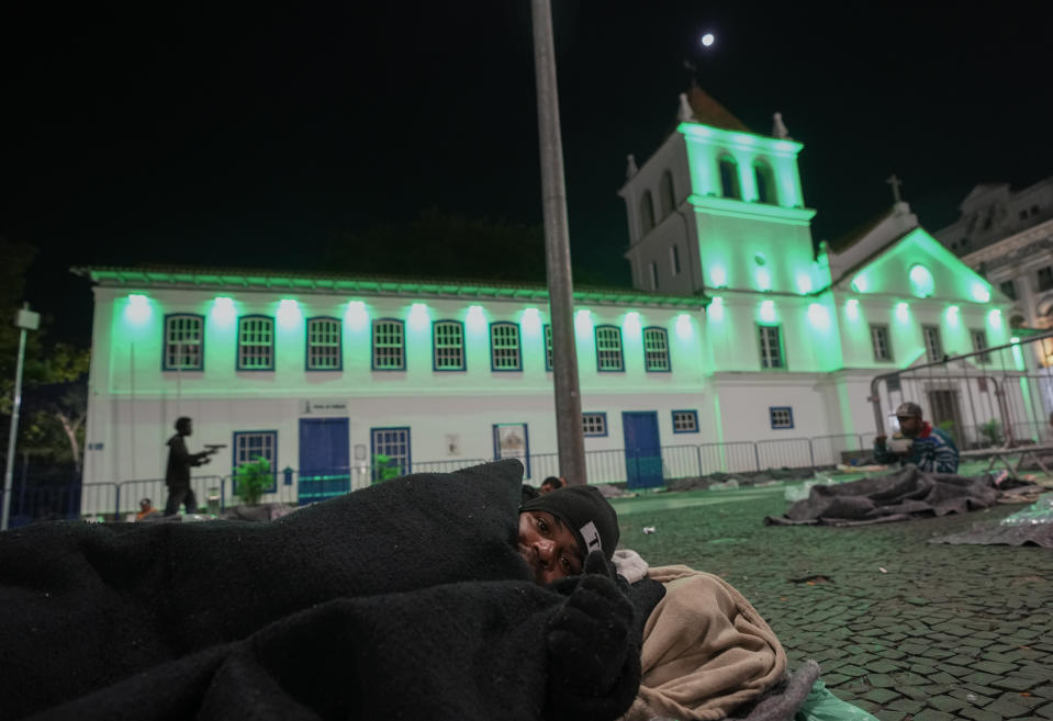 A homeless person prepares to sleep at Patio do Colegio Square during a cold night in downtown Sao Paulo, Brazil, early Friday, May 20, 2022. The homeless population in Sao Paulo has increased 30% during the COVID-19 pandemic, a recent census shows. (AP Photo/Andre Penner)