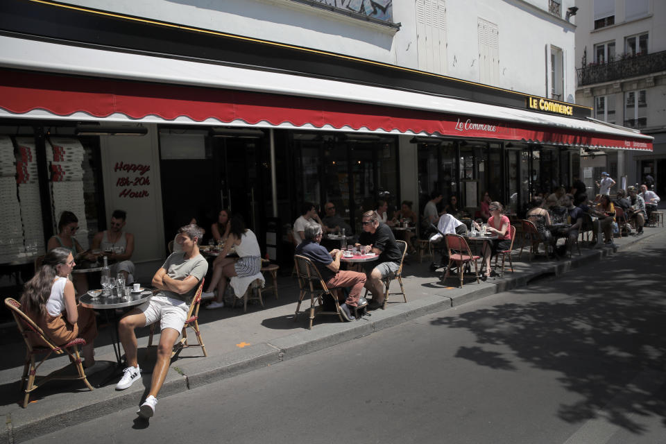 People sit on a terrace in Paris, Tuesday, June 2, 2020. Parisians who have been cooped up for months with take-out food and coffee will be able to savor their steaks tartare in the fresh air and cobbled streets of the City of Light once more, albeit in smaller numbers. (AP Photo/Christophe Ena)