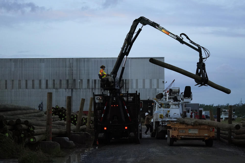 Utility poles are loaded onto trucks at dawn before heading out to restore power, at a tent city for electrical workers in Amelia, La., Friday, Sept. 17, 2021. In the wake of hurricanes, one of the most common and comforting sites is the thousands of electric workers who flow into a battered region when the winds die down to restore power and a sense of normalcy. (AP Photo/Gerald Herbert)