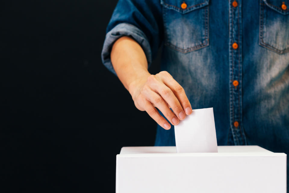 Front view of person holding ballot paper casting vote at a polling station for election vote in black background