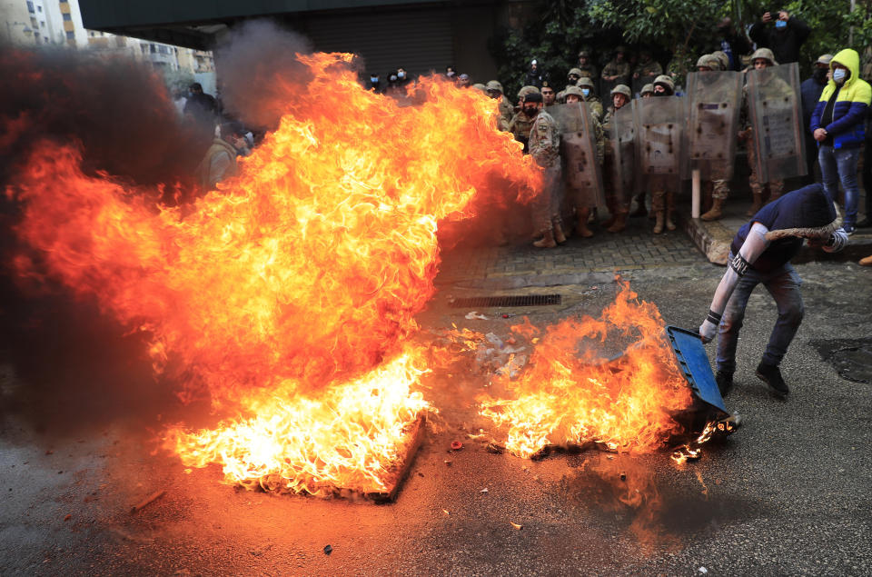 A protester sets a garbage container on fire in front of Lebanese army soldiers, during a protest against deteriorating living conditions and strict coronavirus lockdown measures, in Tripoli, north Lebanon, Thursday, Jan. 28, 2021. Violent confrontations between protesters and security forces in northern Lebanon left a 30-year-old man dead and more than 220 people injured, the state news agency said Thursday. (AP Photo/Hussein Malla)