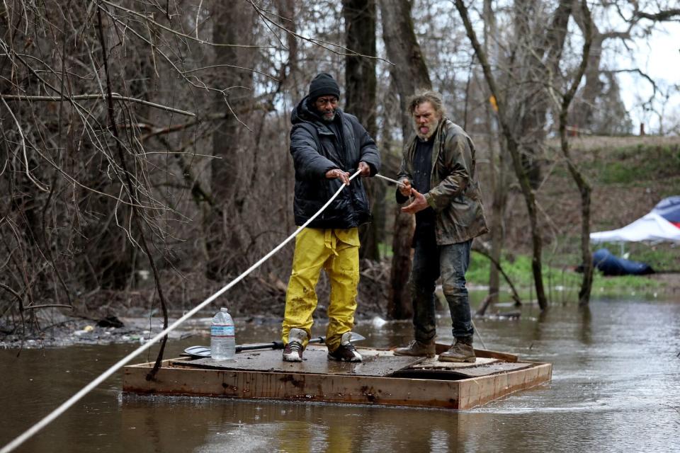 Two men use a raft to get back and forth from the roadway to a homeless encampment