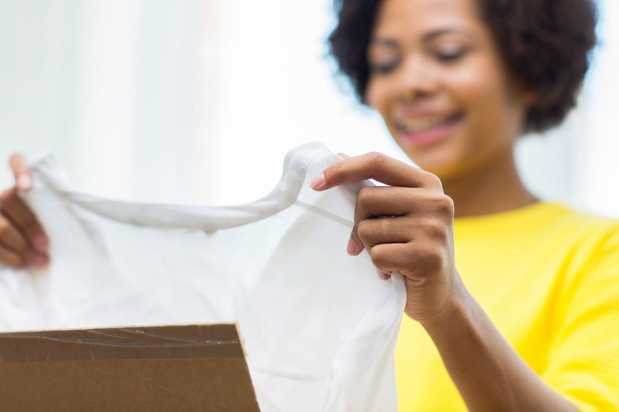 Young woman in bright yellow shirt happily unpacking a box at home