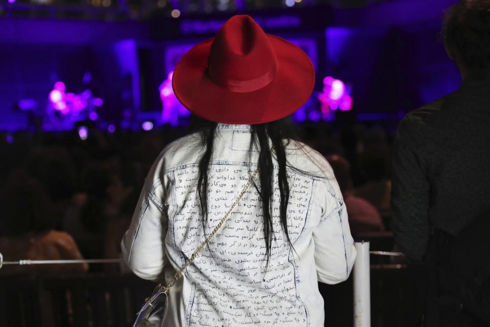 In this Thursday, July 25, 2019 photo, a woman in a jacket with Farsi words, watches a concert of the Tirgan summer festival opening ceremony at the Harbourfront Centre in Toronto, Canada. The event aims to preserve and celebrate Iranian and Persian culture, said festival CEO Mehrdad Ariannejad. Among those who attended were second-and third-generation immigrants, many of whom have never been to Iran or have not been there since leaving the country following the 1979 Islamic Revolution. (AP Photo/Kamran Jebreili)