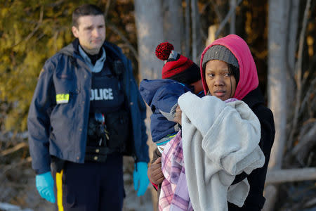 A Royal Canadian Mounted Police (RCMP) officer looks on as a woman carrying a child waits to cross the US-Canada border into Canada in Champlain, New York, U.S., February 14, 2018. Picture taken February 14, 2018. REUTERS/Chris Wattie