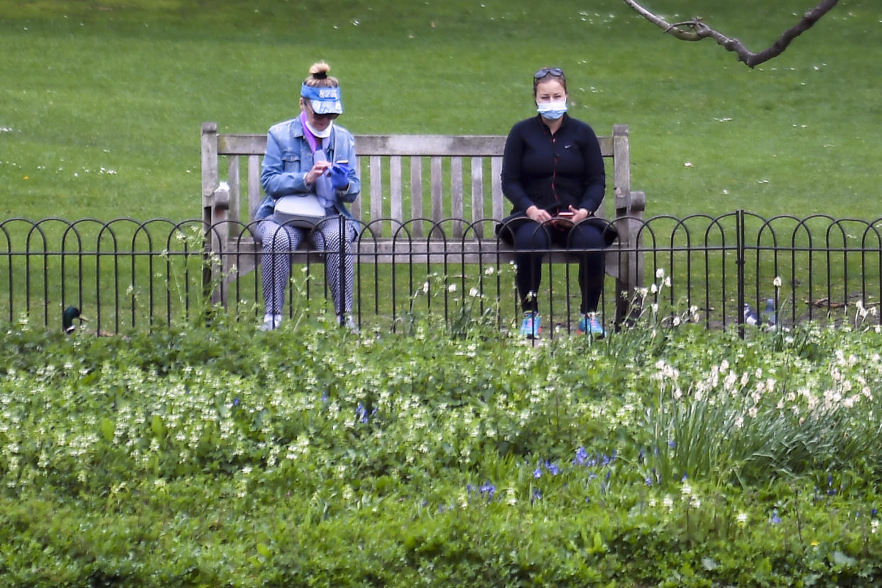 Two people sit on a bench as they wear protective masks and practice social distancing, during lockdown due to the coronavirus outbreak, at St James's Park, in London, Thursday, April 16, 2020. The British government is promising to test thousands of nursing home residents and staff for the new coronavirus, as it faces criticism for failing to count care-home deaths in its tally of victims. (AP Photo/Alberto Pezzali)