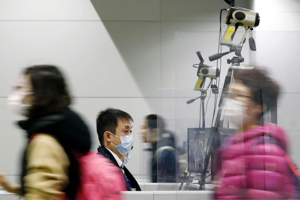 Passengers wearing masks walk by as a quarantine officer, center, monitors a thermography during a quarantine inspection at Kansai international airport in Osaka, western Japan, Wednesday, Jan. 22, 2020. Chinese health authorities urged people in the city of Wuhan to avoid crowds and public gatherings after warning on Wednesday that a new viral illness infecting hundreds of people in the country. Japan, South Korea, the United States and Taiwan have all reported one case each. All of the illnesses were of people from Wuhan or who recently had traveled there. (Kota Endo/Kyodo News via AP)