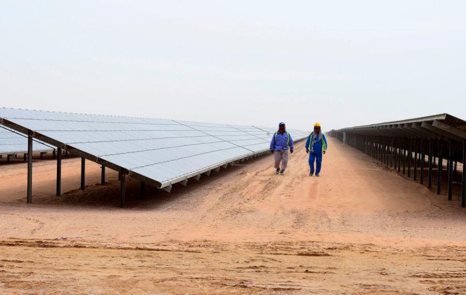 Employees walk past solar panels at the Mohammed bin Rashid Al-Maktoum Solar Park on March 20, 2017, in Dubai. | STRINGER—AFP/Getty Images