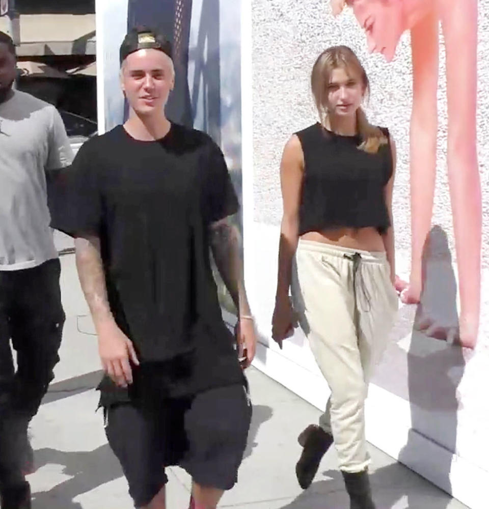Justin Bieber in a casual t-shirt and shorts walks beside Hailey Bieber wearing a crop top and joggers