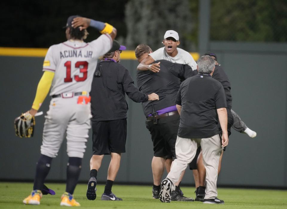 Field guards haul away one of two fans who approached Atlanta Braves right fielder Ronald Acuna Jr. (13) before the bottom of the seventh inning of a baseball game against the Colorado Rockies, Monday, Aug. 28, 2023, in Denver. (AP Photo/David Zalubowski)