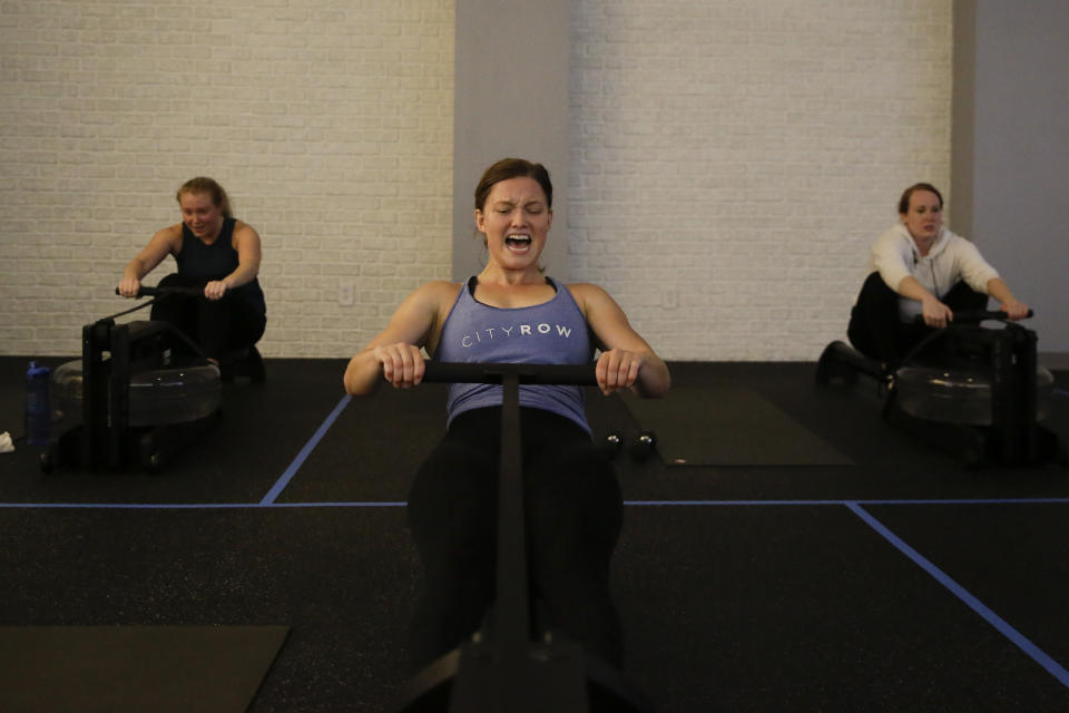 Employee of CITYROW Atlanta Midtown, Ellie Klarl, center, works out as gyms reopen with limited members on Saturday, May 16, 2020, amid the COVID-19 virus in Atlanta. Big box gyms and local fitness studios are reopening under a patchwork of protocols based on state and local guidance, but most are following some basic protocol. (AP Photo/Brynn Anderson)