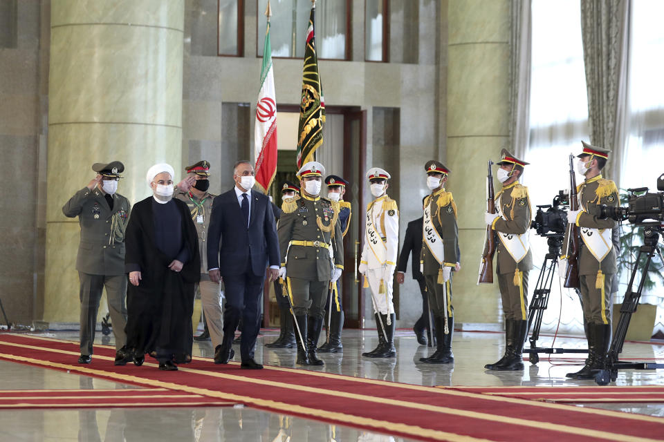 In this photo released by the official website of the office of the Iranian Presidency, Iraqi Prime Minister Mustafa al-Kadhimi, fourth left, reviews an honor guard as he is welcomed by President Hassan Rouhani, second left, as they all wear protective face masks to help prevent spread of the coronavirus, during an official arrival ceremony, in Tehran, Iran, Tuesday, July 21, 2020. (Iranian Presidency Office via AP)