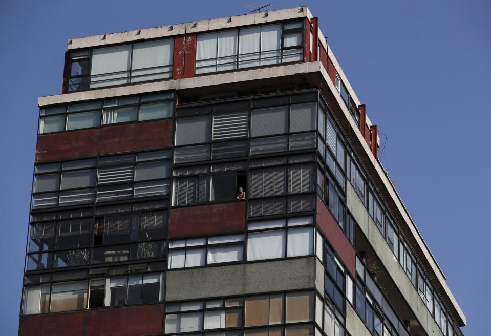 A person peers from the window of an apartment building on Paseo de la Reforma in Mexico City, Thursday, April 23, 2020, as many residents stay home to help contain the spread of the new coronavirus. (AP Photo/Fernando Llano)