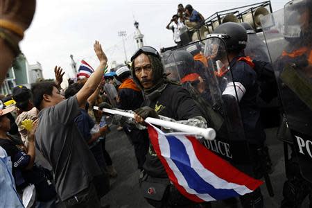 A protester holds a Thai national flag as others face police during a rally against an amnesty bill, on the main road near the government and parliament buildings in central Bangkok November 7, 2013. REUTERS/Damir Sagolj